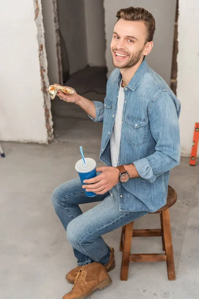 Vista de ángulo alto del joven feliz sosteniendo la taza de papel con bebida refrescante y sonriendo a la cámara en un nuevo hogar - foto de stock