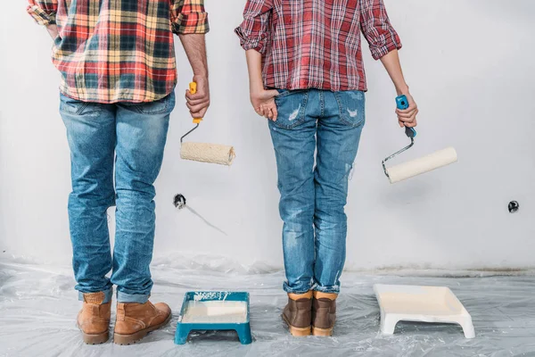 Low section of couple holding paint rollers and painting wall in new house — Stock Photo
