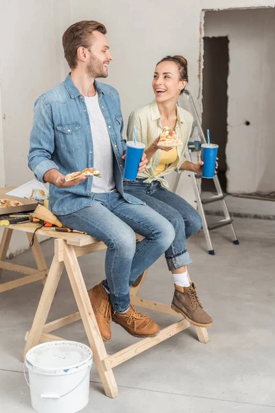 Feliz jovem casal segurando pizza e copos de papel durante a reparação da casa — Fotografia de Stock