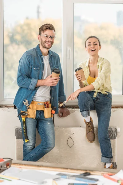 Happy young couple holding coffee to go and smiling at camera during house repair — Stock Photo