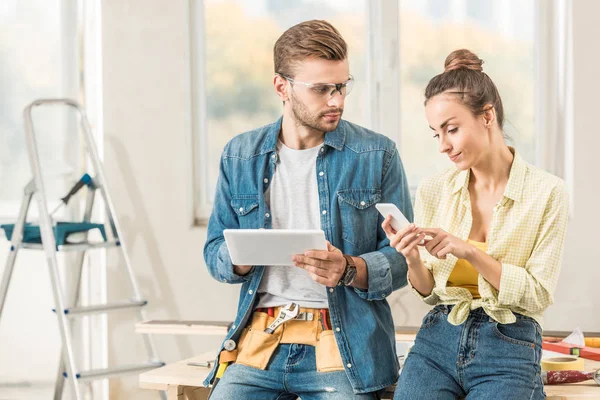 Pareja joven que utiliza dispositivos digitales durante la reparación - foto de stock