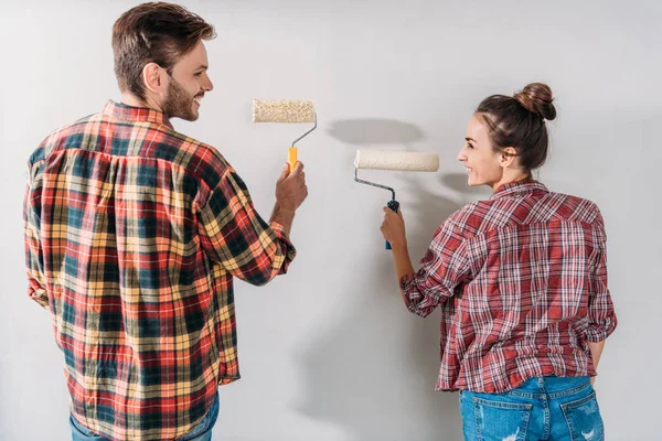 Back view of happy young couple painting wall with paint rollers — Stock Photo