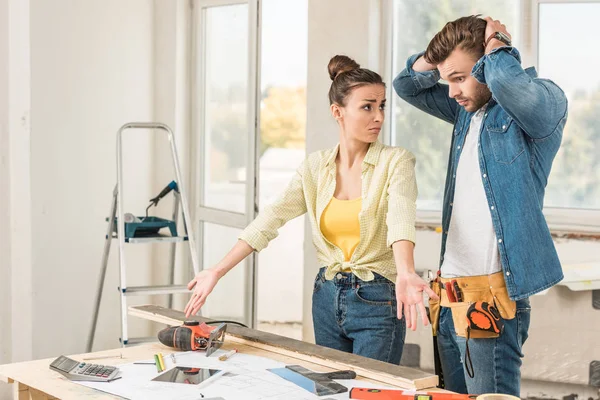 Bouleversé jeune couple debout près de la table avec des outils pendant la réparation de la maison — Photo de stock