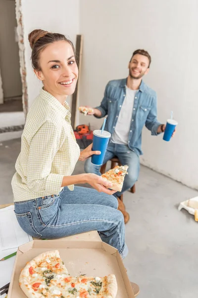 Високий кут зору щасливої дівчини посміхається на камеру, їдячи піцу з чоловіком в новій квартирі — стокове фото