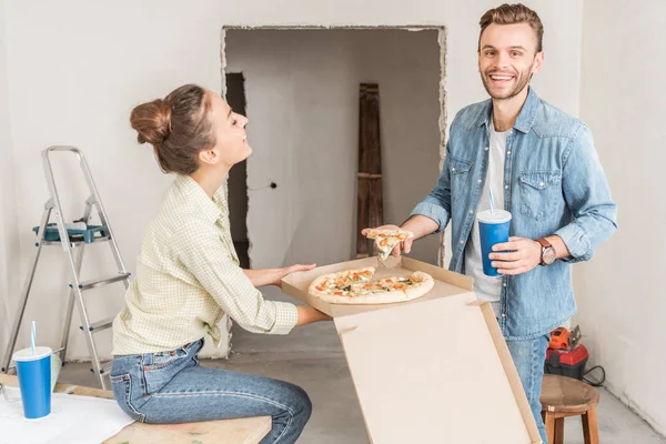 Feliz joven pareja comiendo pizza durante la reparación en nuevo apartamento - foto de stock