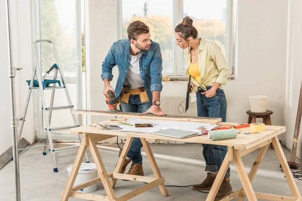 Junge Frau sieht Ehemann bei Reparatur mit elektrischer Stichsäge an — Stockfoto