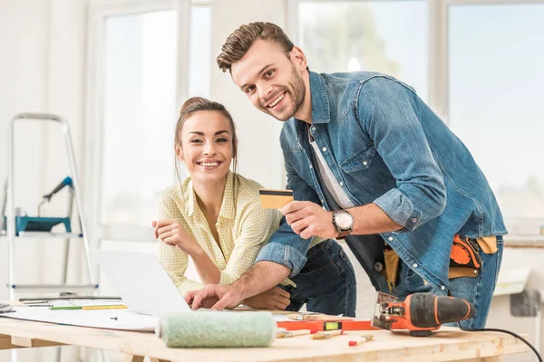 Feliz joven pareja con tarjeta de crédito sonriendo a la cámara durante la mejora del hogar — Stock Photo