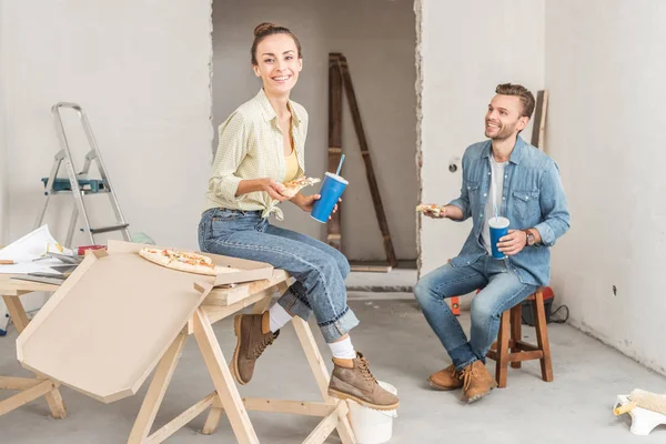 Happy young couple holding pizza slices and paper cups during renovation — Stock Photo