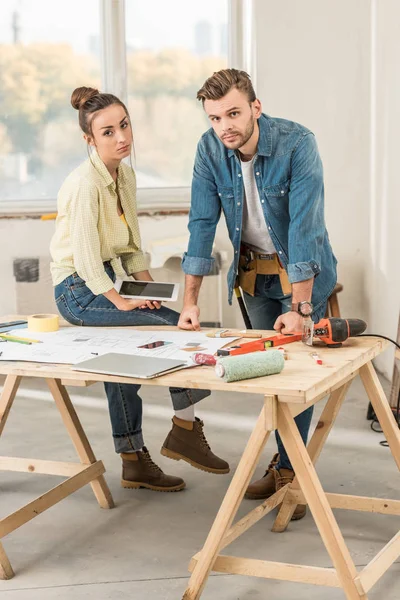 Aufgebrachtes junges Paar lehnt mit Werkzeug am Tisch und blickt bei Renovierung in Kamera — Stockfoto