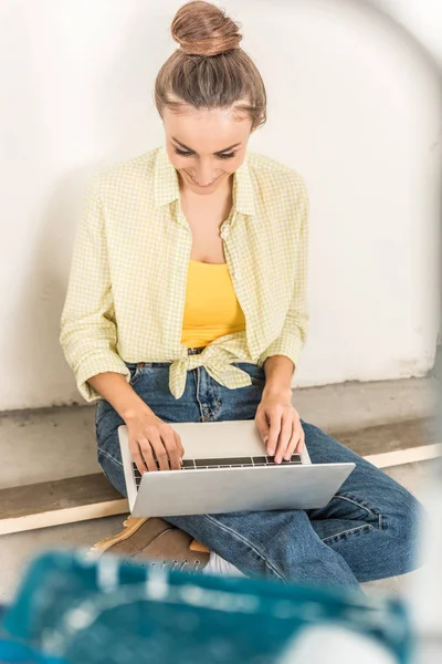 Высокий угол зрения улыбающаяся молодая женщина с помощью ноутбука, сидя в новом доме — стоковое фото