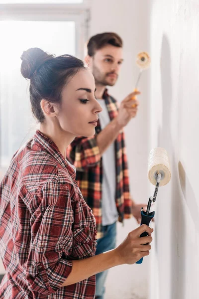 Vista laterale della giovane coppia pittura muro insieme nel nuovo appartamento — Foto stock