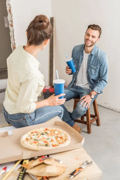 Vista ad alto angolo di giovane coppia in possesso di bicchieri di carta e mangiare pizza durante la pausa nella riparazione — Foto stock