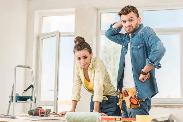 Pareja joven incierta de pie cerca de la mesa con herramientas durante la reparación — Stock Photo