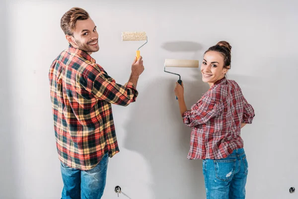 Back view of happy young couple painting wall and smiling at camera — Stock Photo