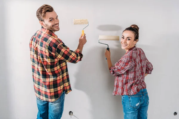 Vue arrière du mur de peinture heureux jeune couple et souriant à la caméra — Photo de stock