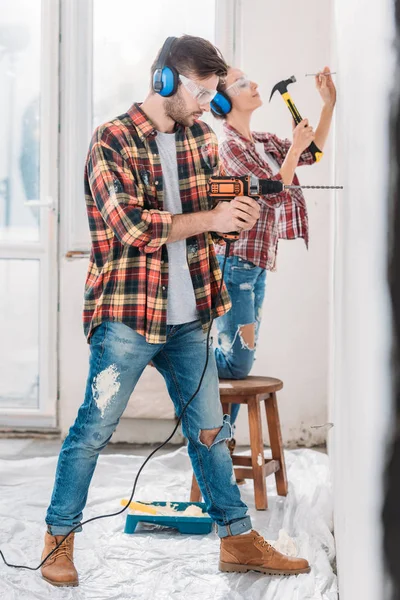 Side view of young couple drilling and hammering wall during renovation — Stock Photo