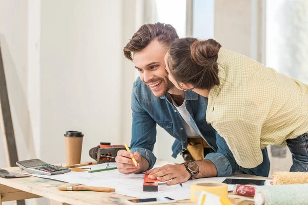 Young woman kissing happy boyfriend marking blueprint with level tool during renovation — Stock Photo