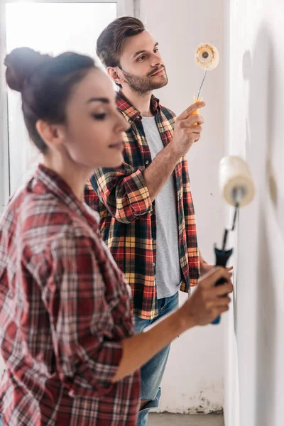 Vue latérale du mur de peinture de jeune couple avec des rouleaux de peinture — Photo de stock