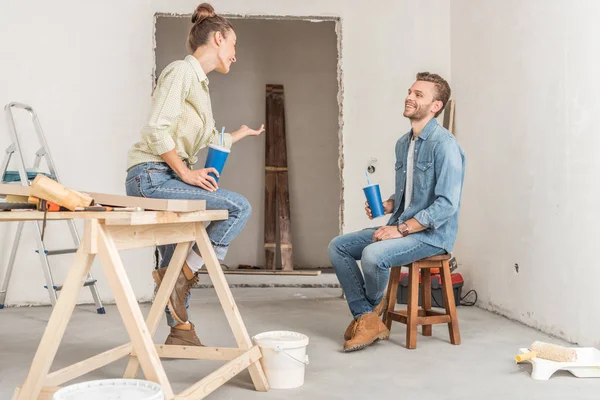 Feliz pareja joven sosteniendo vasos de papel y hablando durante la reparación - foto de stock