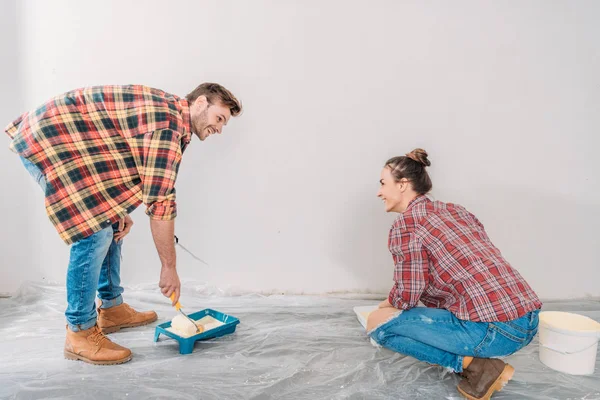 Feliz parede de pintura jovem casal com rolos de pintura e sorrindo uns aos outros — Fotografia de Stock