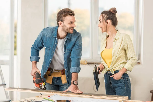 Feliz joven pareja sosteniendo herramientas y sonriendo entre sí durante la reparación - foto de stock