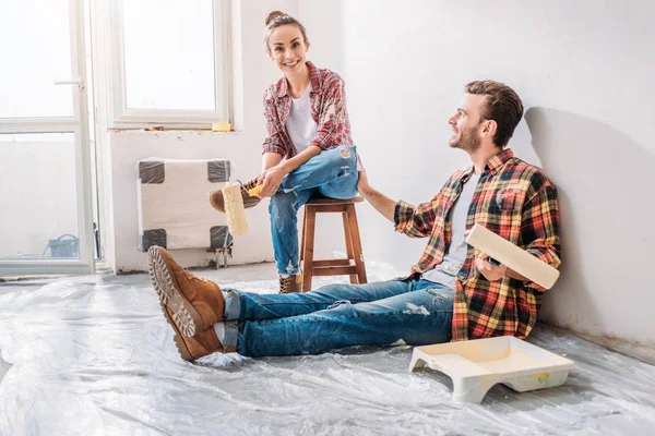 Feliz jovem casal segurando rolos de pintura e descansando durante a reparação — Fotografia de Stock