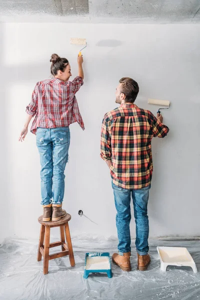 Back view of happy young couple painting wall with paint rollers — Stock Photo