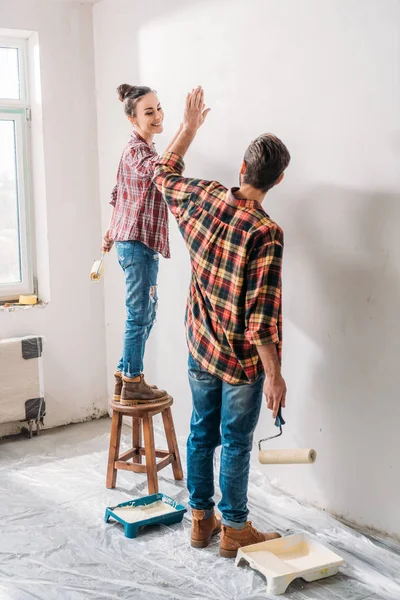 Vista de ángulo alto de la pareja joven dando alta cinco mientras que la pintura de la pared en el nuevo apartamento - foto de stock