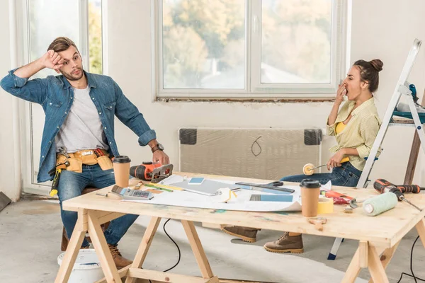 Уставшая молодая пара сидит за столом с инструментами во время ремонта дома — стоковое фото