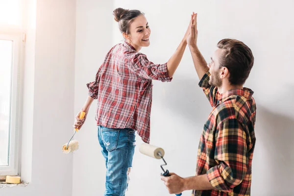 Счастливая молодая пара дает высокую пятерку при покраске стены в новой квартире — стоковое фото