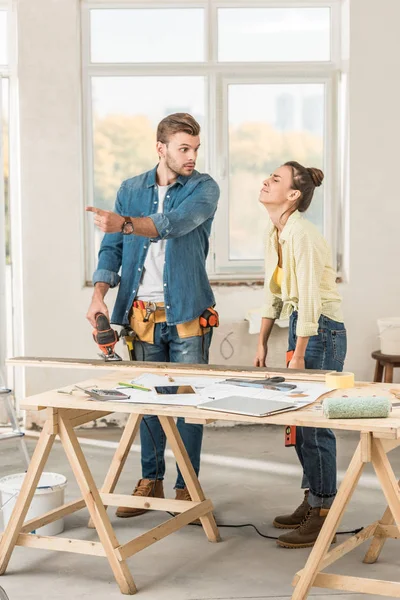 Jeune homme tenant perceuse électrique et pointant du doigt pour contrarier femme pendant la réparation — Photo de stock