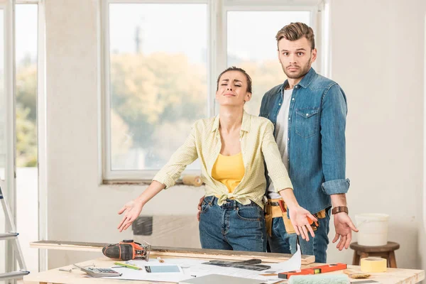 Joven pareja molesta de pie cerca de la mesa con herramientas durante la reparación del hogar - foto de stock