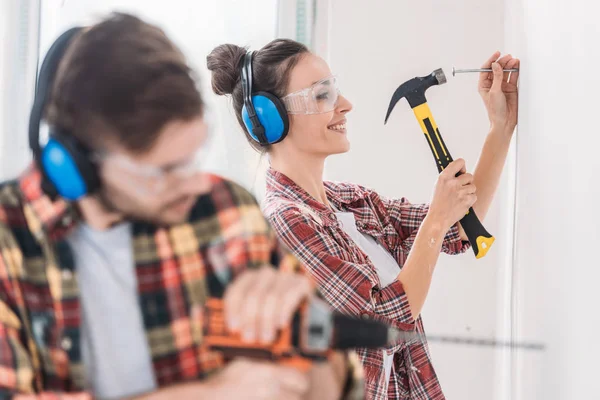 Junges Paar hämmert und bohrt Wand während Renovierung — Stockfoto