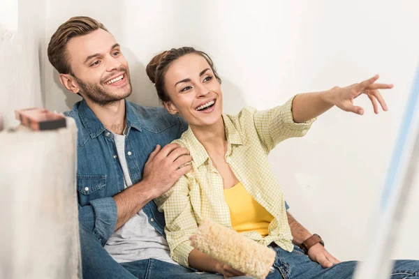 Heureux jeune couple pointant du doigt et détournant les yeux lors de la réparation dans le nouvel appartement — Photo de stock
