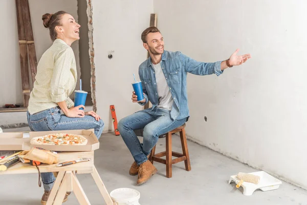 Feliz joven pareja sosteniendo vasos de papel y discutiendo la reparación en nuevo apartamento — Stock Photo