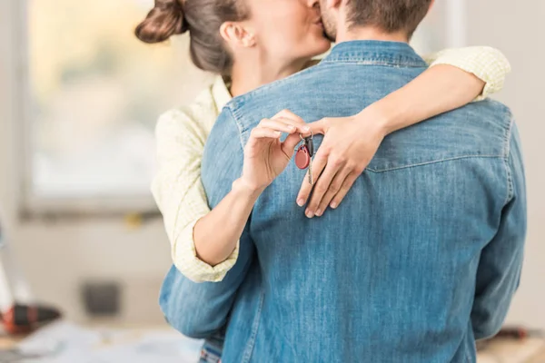 Schnappschuss von glücklicher junger Frau, die Ehemann umarmt und küsst, während sie Schlüssel aus neuer Wohnung hält — Stockfoto