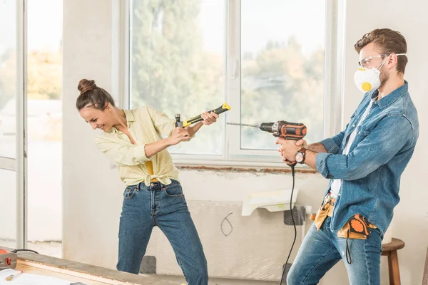 Feliz joven pareja divirtiéndose con herramientas durante la reparación en nuevo apartamento - foto de stock