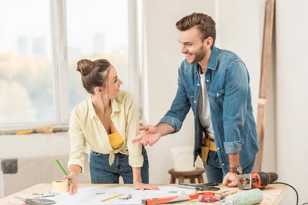 Feliz jovem casal discutindo projeto e sorrindo uns aos outros durante a renovação — Fotografia de Stock