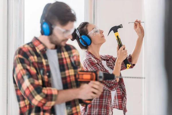 Young couple in protective workwear hammering and drilling wall — Stock Photo