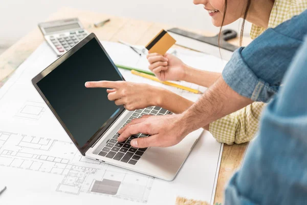 Plan recadré de couple avec carte de crédit à l'aide d'un ordinateur portable avec écran vierge pendant la rénovation — Photo de stock