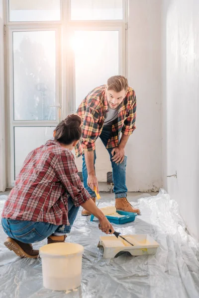 Pareja joven en camisas a cuadros sosteniendo rodillos de pintura y pared de pintura - foto de stock