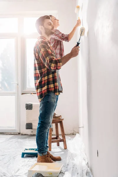 Vista laterale della giovane coppia pittura muro in nuova casa — Foto stock