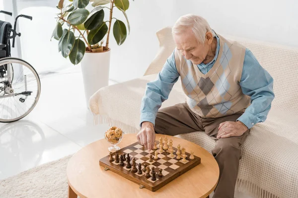 Senior man sitting on sofa and playing chess — Stock Photo