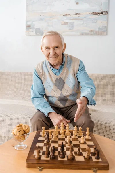 Sonriente hombre mayor sentado en el sofá y jugando al ajedrez - foto de stock