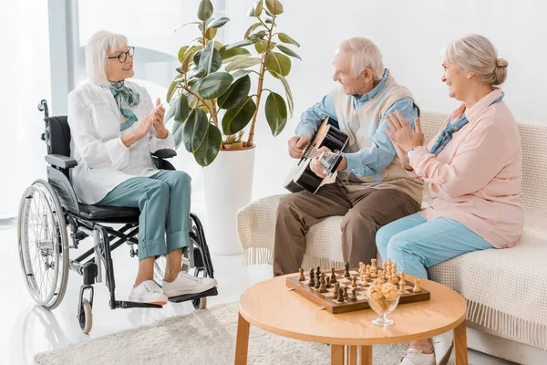 Älterer Mann sitzt auf Sofa und spielt Akustikgitarre für Frauen — Stockfoto