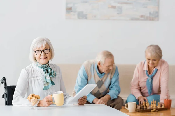 Donna anziana che beve tè con biscotti mentre la coppia anziana gioca a scacchi — Foto stock