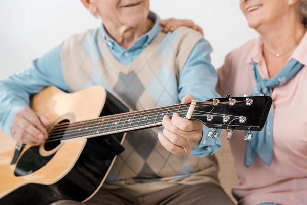 Крупным планом пожилого человека, играющего на акустической гитаре с улыбающейся пожилой женщиной — стоковое фото