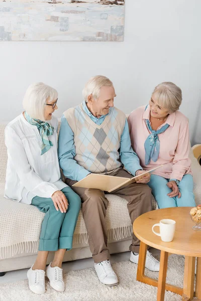 Pessoas alegres seniores sentadas no sofá e lendo livro juntos — Fotografia de Stock