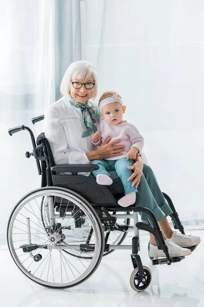 Grand-mère souriante en fauteuil roulant tenant petite petite-fille — Photo de stock