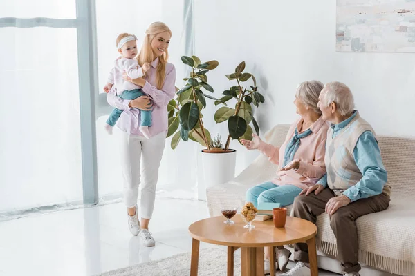 Young woman holding toddler while senior people sitting on sofa — Stock Photo